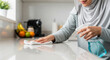 © Nii_Anna - Muslim woman cleaning kitchen counter with spray bottle and cloth