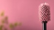 © STK - Macro view of a mascara wand applicator on a soft pink backdrop featuring blurred green foliage.