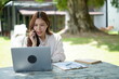 © TesLaTH - Woman working outdoors on a laptop, engaged in calls.