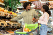 © Prostock-studio - A cheerful couple shops in a grocery store, picking out fresh fruits. They share smiles while examining fresh produce in well-stocked displays.