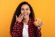 © Prostock-studio - A joyful woman laughs while holding a tasty burger, enjoying her cheat meal. She wipes her lips with her finger, captured against a bright orange background that enhances her excitement.