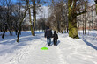 © Anastasiia - Man walking with child and pulling green sled in snowy urban park. Winter outdoor activity.