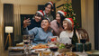 © tirachard - Group of Asia colleague gathering New year holidays party together. Happy friend group mobile phone video call online christmas thanksgiving dinner at home in evening, celebration and people concept.