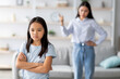 © Prostock-studio - In a living room, a daughter stands with crossed arms, ignoring her mother who appears frustrated. The girl shows her displeasure, emphasizing the family conflict between them.