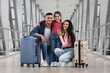 © Prostock-studio - A happy family of three stands together in an airport terminal, smiling and posing with their luggage. They look excited about their upcoming trip. The space is bright and modern.