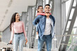 © Prostock-studio - A father carries his daughter on his shoulders while a woman walks beside them, all smiling as they prepare for a journey at the airport terminal.