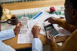 © pressmaster - Middle aged Black man and middle aged Black woman reviewing tax documents together at table, using calculator and receipts, discussing financial paperwork related to paying taxes