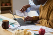 © pressmaster - Middle aged Black man using laptop while reviewing financial documents with middle aged Black woman assisting, both focusing on paying taxes at home office table with paperwork and calculator