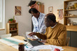 © pressmaster - Middle aged Black man using laptop and reviewing tax documents with young Black woman standing beside him assisting with paperwork related to paying taxes