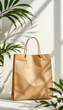 © NAD SANG PAP - Brown shopping bag with handles standing on white surface with green plant shadows and sunlight in background