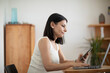 © Connect Images - Woman using smartphone and laptop at a wooden table in a cozy, modern indoor setting. Germany