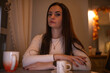 © shymar27 - Young woman with long dark hair sits at a table, hands clasped, in a cozy cafe setting, warm lighting creating an inviting atmosphere for conversation and relaxation