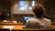 © Golden boy - Student sits alone in lecture hall, focused on laptop while presentation plays in background. atmosphere is quiet and contemplative, highlighting learning experience