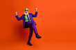 © deagreez - Elderly man in a purple suit dancing with joy against a bright orange background wearing a green shirt and sunglass