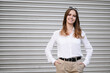 © GRON777 - Female entrepreneur in city against silver city wall. Welcoming, confident, and approachable businesswoman, portrait of founder, entrepreneur demonstrating leadership qualities