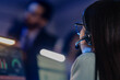 © ultramansk - Close-up rear view of young female operator wearing headset with microphone in blue-lit room, managing communication for customer support or online gaming session.