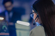 © ultramansk - Close-up rear view of young female operator wearing headset with microphone in blue-lit room, managing communication for customer support or online gaming session.