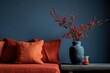 © gamespirit - A charming corner of the living room features bright orange cushions and delicate berry branches arranged in a striking dark blue vase, set against a vibrant wall.