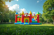 © Viktor - Bright inflatable bounce house castle in park with green grass under sunny blue sky. Colorful playground equipment for kids. Family event fun activities outside