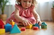 © Viktor - Cute child playing with colorful wooden blocks on the floor in room. Girl develops creative skills, fine motor. Early learning concept. Kid builds from geometric toy figures at home.