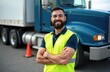 © Viktor - Smiling bearded man in yellow safety vest poses near a semi truck. Truck driver with crossed arms. Pro truck driving school training. Career change concept logistic transportation.