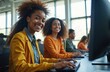 © Viktor - Smiling young African American women learn in modern computer lab. Diverse students use tech for education, research. Work together on computers, studying in college classroom university office today.