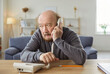 © Studio Romantic - Serious mature man having conversation, holding handset near ear, making telephone call, has bored expression, focused away, posing against home interior, has free time for talking