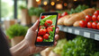 © Viktor - Person holds smartphone looking at food photo in market. Closeup hand with mobile device near vegetables. Online grocery shopping app on screen for ordering healthy food.