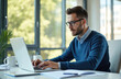 © Viktor - Young businessman in glasses works on laptop at office desk. Types on keyboard, deeply focused on planning important business strategy. Pro male concentrates on daily tasks in modern, bright
