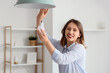 © Pixel-Shot - Pretty young woman changing light bulb of hanging lamp at home