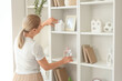 © Pixel-Shot - Female interior designer decorating shelving unit with figurines in stylish room