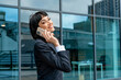 © Iryna - Businesswoman smiles while talking on phone outside modern office building in the city during daytime