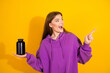 © deagreez - Bright portrait of young woman in a purple hoodie hold black bottle pointing with excitement yellow backdrop lifestyle advertising fashion shopping campaigns