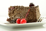 Słodki deser w postaci czekoladowego ciasta z polewą ozdobionego kandyzowanymi wiśniami