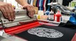 © yevhen89 - Worker hands pushing squeegee with red ink onto screen printing frame creating custom skull design on black t-shirt in print shop