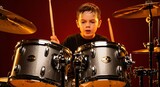 a young boy passionately plays a drum set with focused expression holding drumsticks mid air against a dramatic red background illumination high quality professional detailed modern
