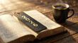 © PhotoGranary - Open book with elegant 2026 bookmark and black coffee cup on a wooden table. Cozy morning atmosphere with warm sunlight and magical golden particles for New Year reading.