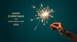 © PhotoArtHub - A hand holding a sparkler, shining bright against a teal background with holiday greetings, representing festive celebration and cheerful occasion