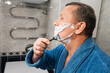 © svetlana_cherruty - Man in blue robe applies shaving cream and shaves with razor in bathroom. Morning Shaving Routine. Close up.