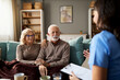 © Goran - Happy mature couple talking with a female nurse during her home visit.