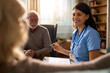 © Goran - Smiling female healthcare worker talking with her mature patients during home visit