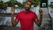 © Krakenimages.com - Man in red t shirt raising hands with bare forearms in front of building stairs and potted plants; thoughtful reflection.
