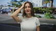 © Krakenimages.com - Young hispanic woman waving hand on street in sunlit urban scene, smiling warmly as she looks ahead; happiness.