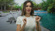 © Krakenimages.com - Woman presents open palm by building beside pool in white shirt, showcasing resort setting; relaxation.