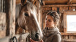 © t.sableaux - Young woman gently brushing horse's mane in rustic stable, warm natural light creating a serene atmosphere of connection and care