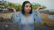 © Krakenimages.com - Woman in blue shirt expressing confusion at beach with blurred background of seaside landscape.