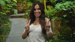 © Krakenimages.com - Woman smiling and showing peace sign with both hands on a green park path, facing camera and wearing a white shirt; joy celebration.