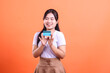 © Ajab - A smiling young woman holds a credit card with her two hands, happy for the new financial possibilities, isolated on orange background.