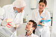 © JackF - During appointment, mature man dentist and girl nurse communicates with male patient, shows model of jaws and explains mechanism of defect formation.