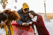 © Xavier Lorenzo - Group of cheerful multi-ethnic friends using mobile phone, having fun together at amusement park during wintertime